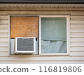 Calgary, Alberta, Canada. Jul 19, 2024. A close-up of a window with a Kenmore air conditioner installed in the lower portion and a wooden board covering the upper half. 116819806