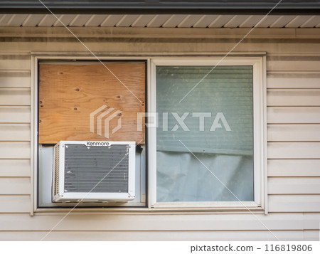 Calgary, Alberta, Canada. Jul 19, 2024. A close-up of a window with a Kenmore air conditioner installed in the lower portion and a wooden board covering the upper half. 116819806