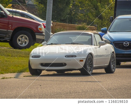 Calgary, Alberta, Canada. Jul 17, 2024. A white Mazda MX-5 Miata parked on a suburban street, its compact and sporty design, features a soft-top roof and custom alloy wheels. 116819810