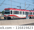 Calgary, Alberta, Canada. Jul 21, 2024. A Calgary C-Train brightly colored in red and white travels along an elevated highway lane separated by concrete barrier. 116819823