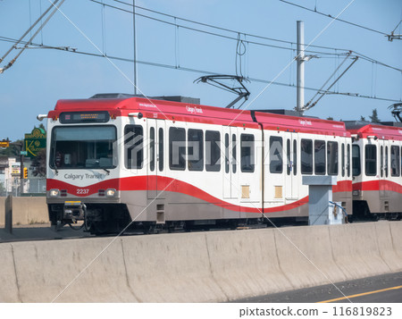 Calgary, Alberta, Canada. Jul 21, 2024. A Calgary C-Train brightly colored in red and white travels along an elevated highway lane separated by concrete barrier. Calgary, Alberta, Canada. Jul 21, 2024. A Calgary C-Train brightly colored in red and white travels along an elevated highway lane separated by concrete barrier. 116819823