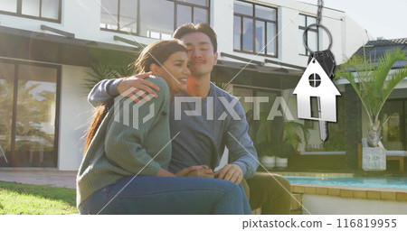 Image of silver house key and key fob over happy diverse couple in garden at home 116819955
