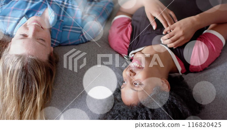 Image of light spots over two happy diverse teenage girls lying o bed talking 116820425