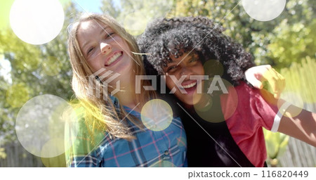 Image of yellow and white light spots over two happy diverse teenage girls embracing in garden Image of yellow and white light spots over two happy diverse teenage girls embracing in garden 116820449