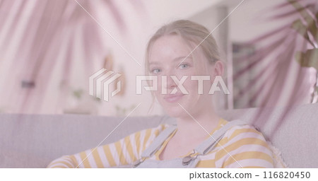 Image of palm leaves over smiling caucasian teenage girl relaxing at home 116820450