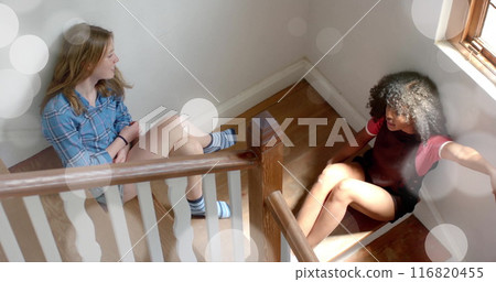 Image of white light spots over two diverse teenage girls siting on stairs talking at home Image of white light spots over two diverse teenage girls siting on stairs talking at home 116820455