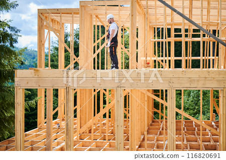 A construction manager is overseeing the building of wooden frame two-story house near the forest. The concept behind it is modern and environmentally friendly construction. 116820691
