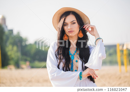Portrait of a young woman with long dark hair in a hat and turquoise jewelry on the beach in summer day. Boho style Portrait of a young woman with long dark hair in a hat and turquoise jewelry on the beach in summer day. Boho style 116821047