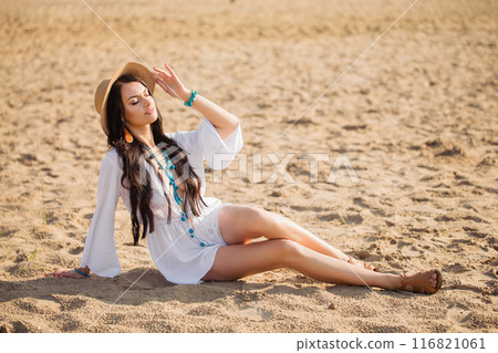A beautiful woman in boho style clothes resting on the sand at the beach on a summer day 116821061