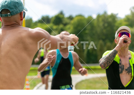 A volunteer holds out a plastic cup of water to a triathlon runner. 116821436