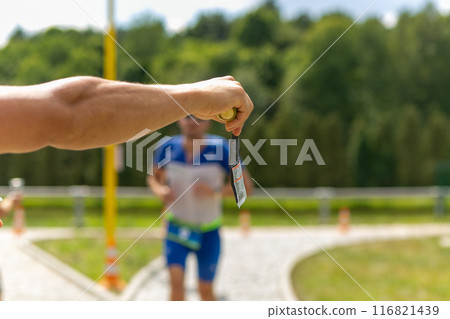 A volunteer holds out a plastic cup of water to a triathlon runner. 116821439