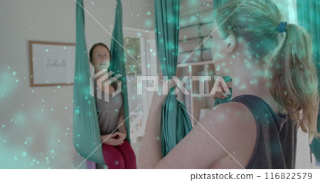 Image of glowing green particles over happy caucasian female aerial yoga teacher and student 116822579