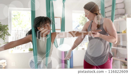 Image of light spots over diverse female instructor and teenage girl practicing aerial yoga 116822609
