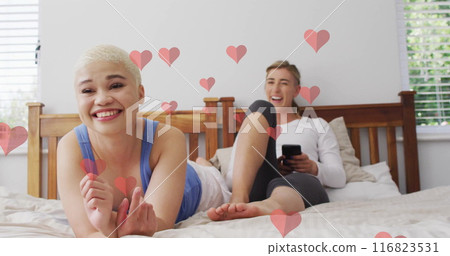 Image of hearts floating over diverse female couple watching tv Image of hearts floating over diverse female couple watching tv 116823531