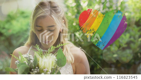 Image of rainbow heart over caucasian woman wearing wedding dress and holding flowers 116823545