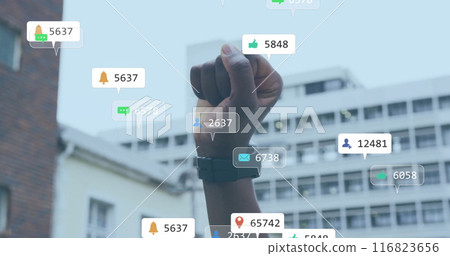 Image of social media notifications over african american woman raising fist in city 116823656