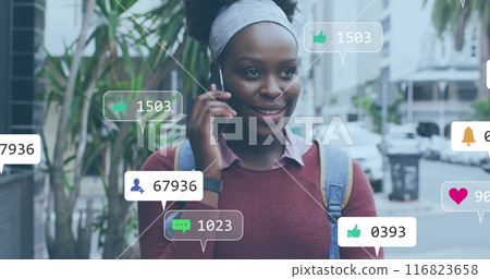 Image of media notifications over african american woman talking on smartphone in city 116823658