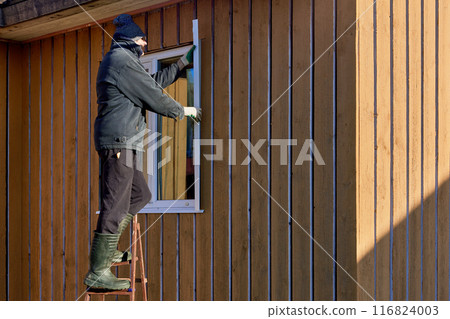 Standing on stepladder, roofing contractor installs metal window slopes on facade side. 116824003