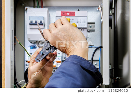 Electrical installation work on connecting power cable to an outdoor electrical cabinet, installer cleans ends of wires from insulation using stripper cutter tool. Electrical installation work on connecting power cable to an outdoor electrical cabinet, installer cleans ends of wires from insulation using stripper cutter tool. 116824010