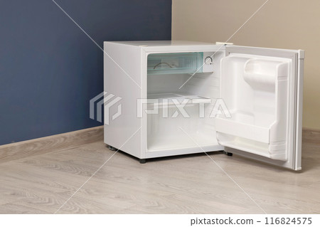 Single chamber empty white open mini fridge with freezer above on floor. Home appliances. Food and food storage at home.  116824575