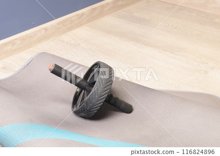 Fitness gymnastic wheel with two handles on mat in room. Equipment for sports activities. Health and movement. Fitness gymnastic wheel with two handles on mat in room. Equipment for sports activities. Health and movement. 116824896