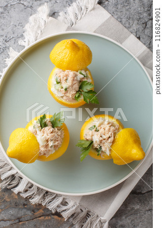 Fresh lemons stuffed with canned tuna salad with eggs, vegetables and cream cheese close-up in a plate. Vertical top view Fresh lemons stuffed with canned tuna salad with eggs, vegetables and cream cheese close-up in a plate. Vertical top view 116824901