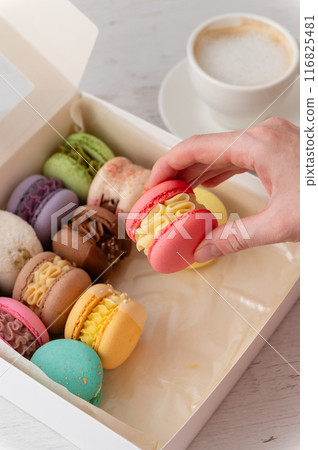 A woman's hand takes out a delicious macaroon from a box. A woman's hand takes out a delicious macaroon from a box. 116825481