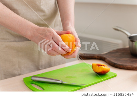 A female hand cuts a tasty juicy peach. A female hand cuts a tasty juicy peach. 116825484