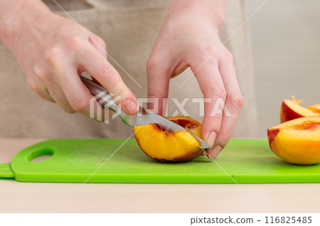 A female hand cuts a tasty juicy peach. A female hand cuts a tasty juicy peach. 116825485