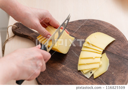 A woman cuts cheese into thin slices. A woman cuts cheese into thin slices. 116825509
