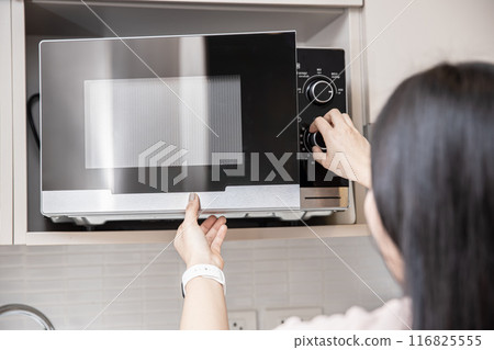 people using the microwave oven, women adjust time to reheat warm food in microwave. 116825555