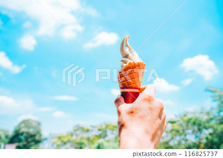 A man's hand holding a soft serve ice cream against the blue sky 116825737