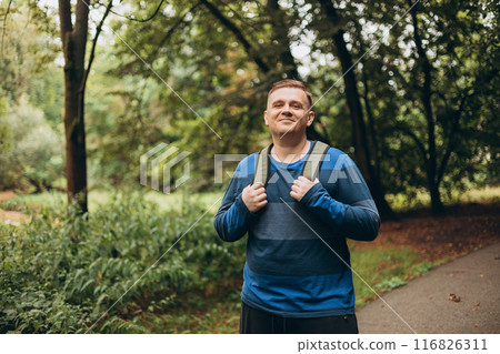 Happy man with backpack standing outside. One Caucasian male hiking in the woods. Travel, active lifestyle, people concept. Traveler enjoys eco-tourism, nature walks. 116826311