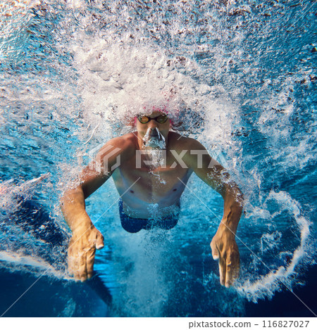 Focused swimmer, seen underwater during training, wears pink cap and goggles, his powerful strokes creating dynamic water movement. 116827027