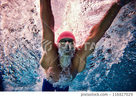 Photo of athletic male swimmer, sportsman wearing pink cap and goggles, training in pool his skills underwater. Photo of athletic male swimmer, sportsman wearing pink cap and goggles, training in pool his skills underwater. 116827029