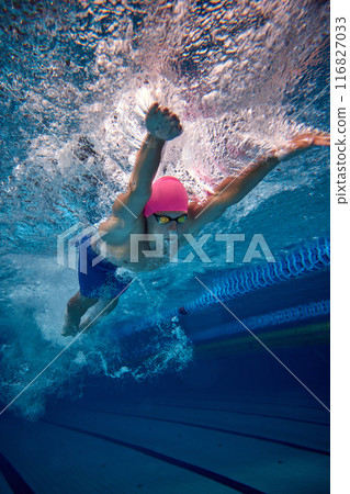 Male swimmer, highlighting his efficient freestyle technique, wearing blue trunks and goggles in pool underwater. 116827033