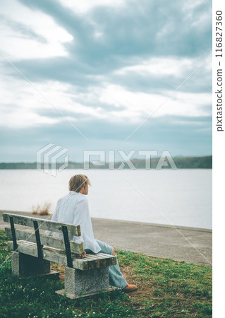 Back view of a light brown-haired man sitting on a bench looking at the sea 116827360