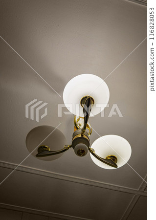 Vertical shot of chandelier with three lamps, one of which does not illuminate. Symbol of trinity in which balance is disturbed and one element has failed. Signals, symbolism, closed sacred knowledge Vertical shot of chandelier with three lamps, one of which does not illuminate. Symbol of trinity in which balance is disturbed and one element has failed. Signals, symbolism, closed sacred knowledge 116828053