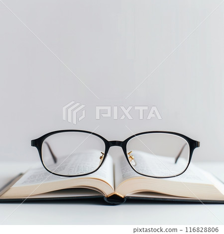 Black eyeglasses rest on an open book against a white background. 116828806