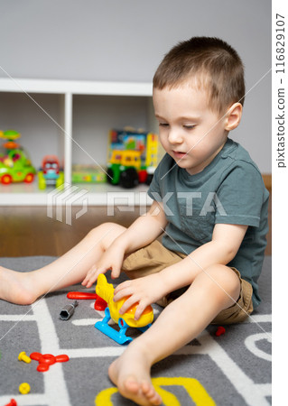 A little toddler boy 2.5 years is playing with a toy helicopter, assembling and disassembling it. Educational toys for kids. Children's room in home. Indoors 116829107