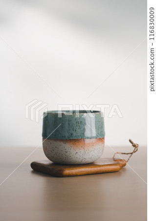 A dual-glazed ceramic cup rests on wood. 116830009