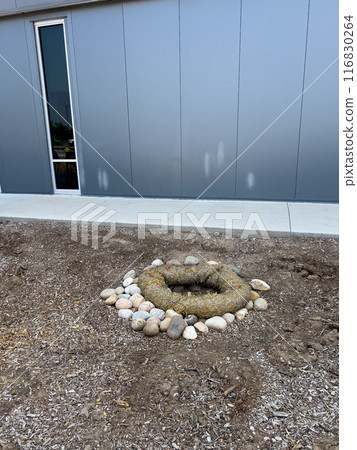 This image depicts an outdoor drainage system protected by erosion control measures. The drain is surrounded by a circular barrier made of natural fiber rolls and large river rocks. The setup ensures 116830264
