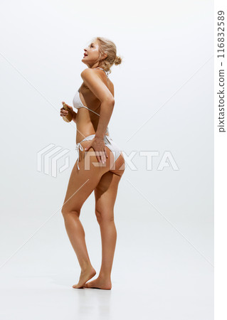 Rear view photo of blonde woman using spray to protect skin in moment of sunbathing against white studio background. 116832589