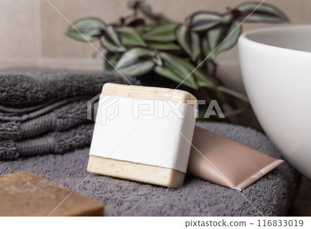 Soap bar with blank label near grey towels, green plant and basin on wood in bathroom, mockup Soap bar with blank label near grey towels, green plant and basin on wood in bathroom, mockup 116833019