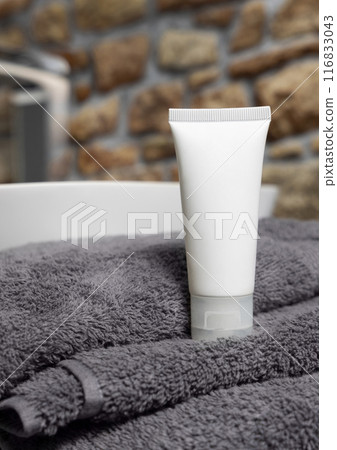 White cosmetic tube on dark grey folded towel near vessel basin against stone wall, mockup White cosmetic tube on dark grey folded towel near vessel basin against stone wall, mockup 116833043