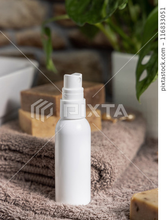 White spray bottle on brown towels near sink and green plant close up, cosmetic mockup 116833051