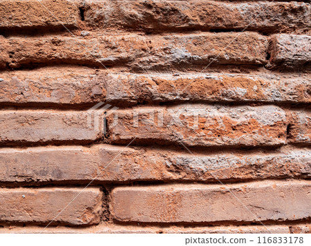 A close-up shot of a weathered red brick wall, featuring rows of bricks laid horizontally. A close-up shot of a weathered red brick wall, featuring rows of bricks laid horizontally. 116833178