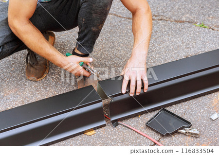 After bending aluminum rain gutters on machine tool, worker cuts them with shears to required size 116833504