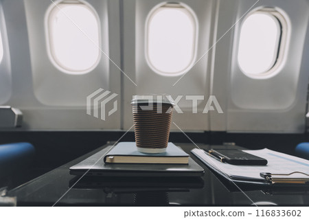 Cup of coffee with laptop and notebooks on table in airplane Cup of coffee with laptop and notebooks on table in airplane 116833602
