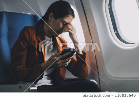 Stressed and serious young asian businesswoman remote working on the plane, suffering from headache and airsick during the flight. 116833640